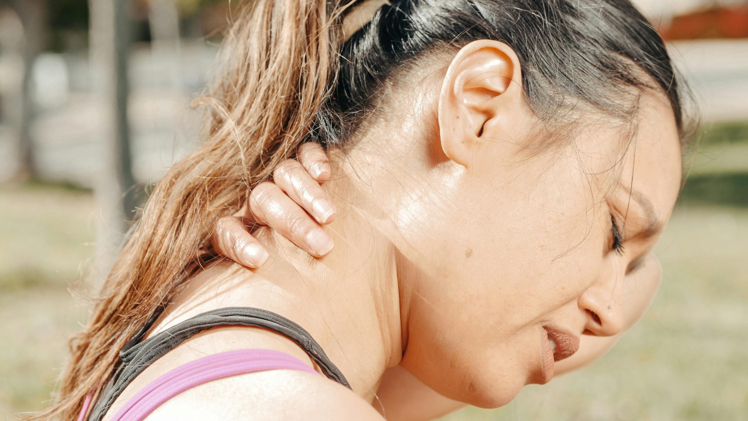 woman wincing in pain, holding the back of her neck