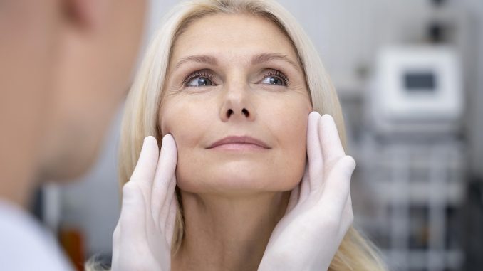 cosmetic surgeon gently lifting a patient's facial skin, evaluating for a facelift